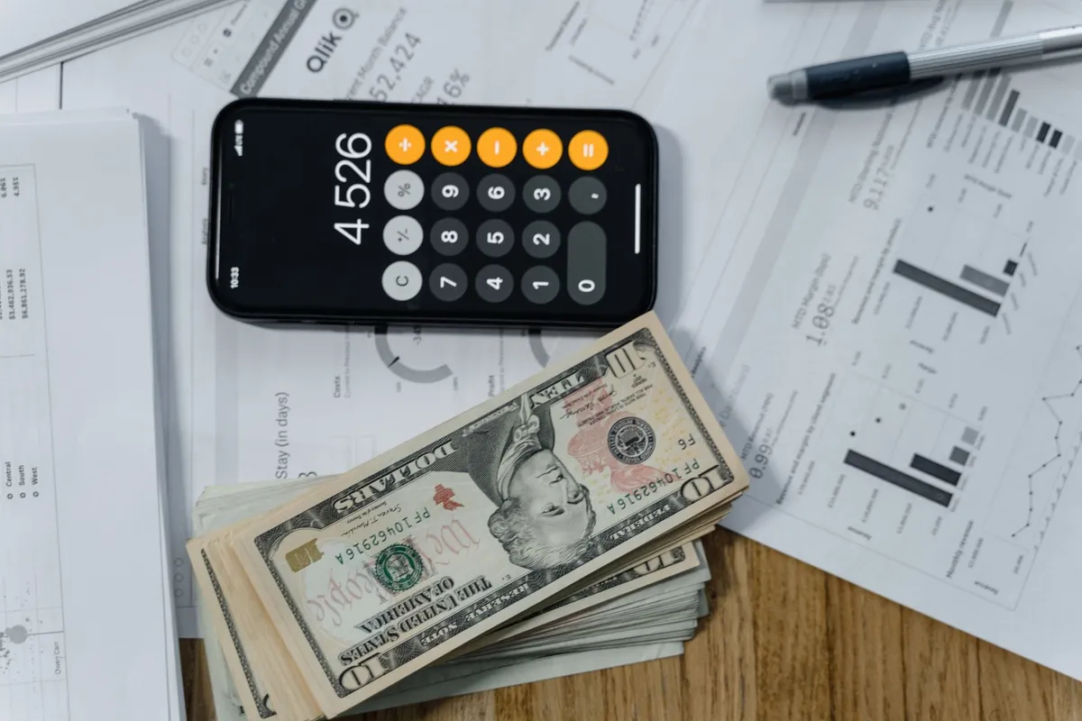A mobile calculator, cash, and financial documents on a desk, symbolizing business planning and bookkeeping.