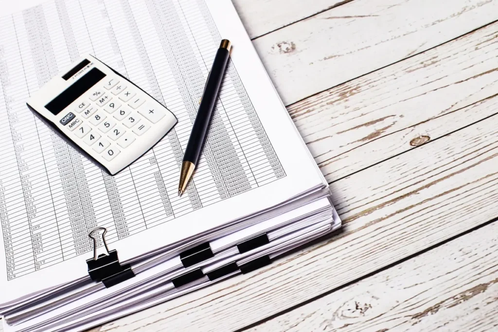 A white calculator and pen on a stack of documents, symbolizing the need for bookkeeping services.